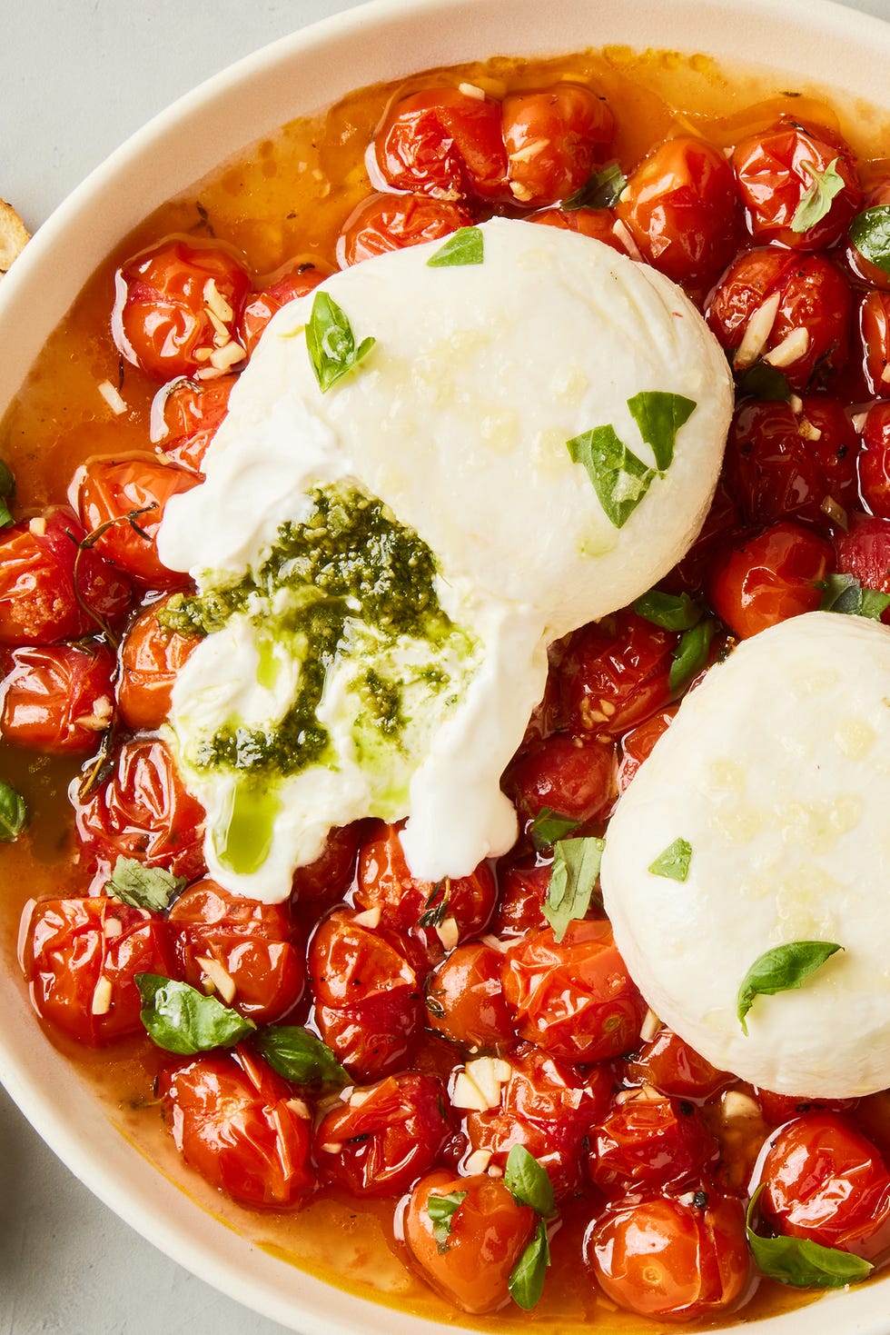 Pesto Stuffed Burrata Bombs pesto stuffed burrata on top of burst cherry tomatoes with basil