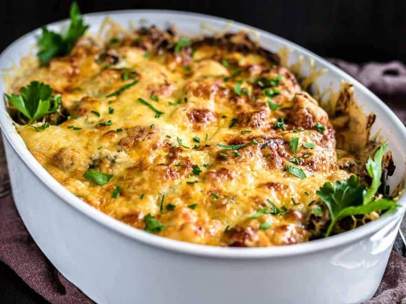 A baked casserole in a white dish topped with melted golden cheese and garnished with fresh parsley.