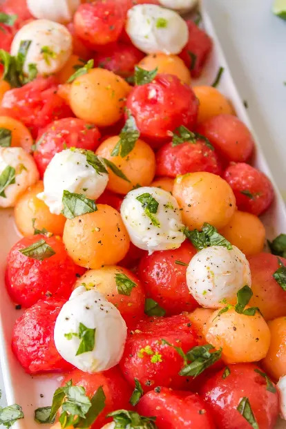 Mixed melon balls with mozzarella and fresh herbs on a white platter