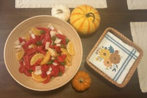 Red pepper and orange salad prepared and set on the table with autumn decor including three small pumpkins. 