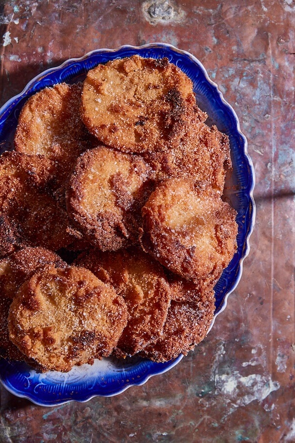 A blue plate filled with round, golden-brown apple fritters coated in sugar, placed on a marbled surface, evokes a sense of nostalgia.