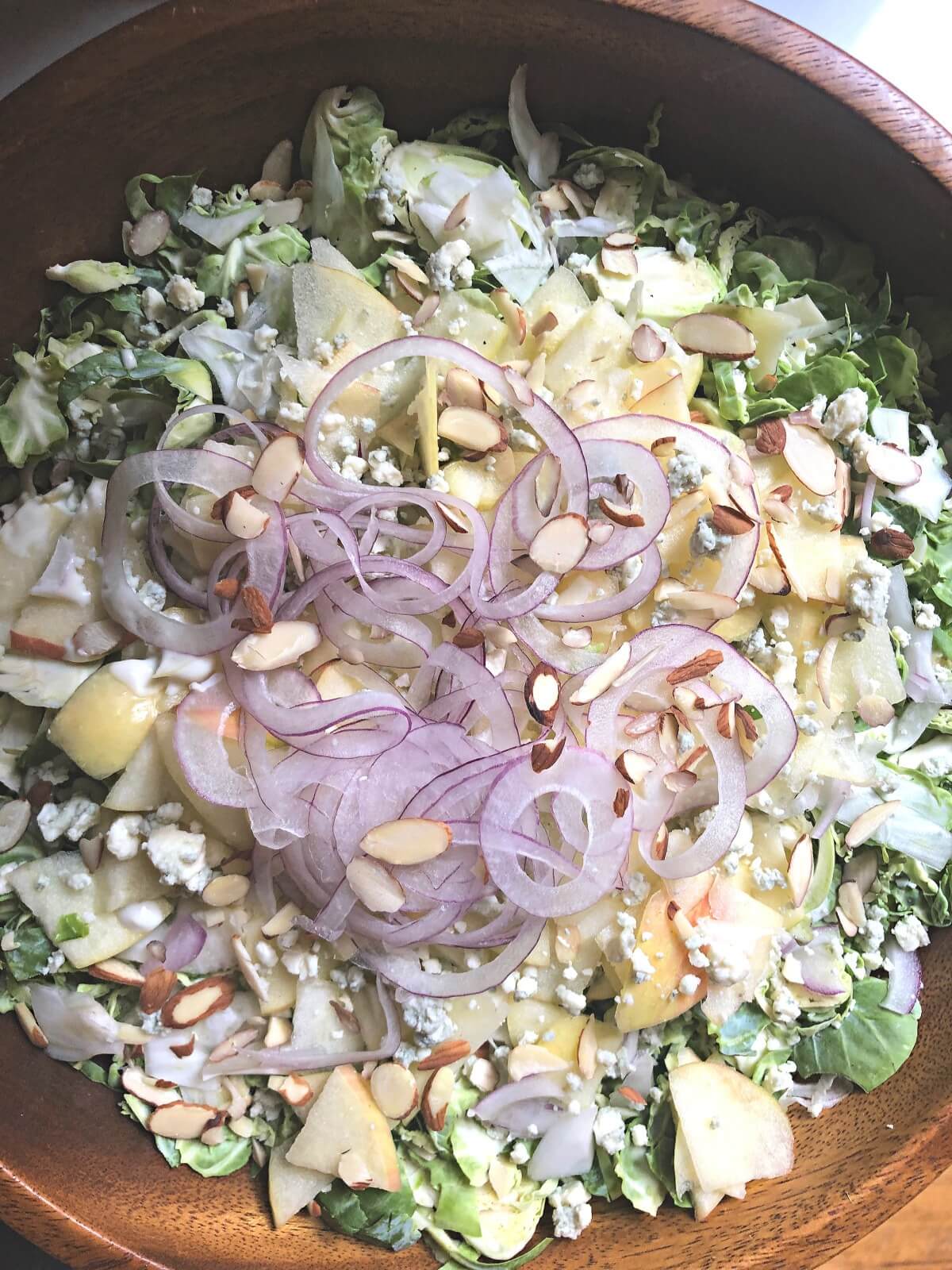 overhead view of salad with greens, apples, nuts, and red onions