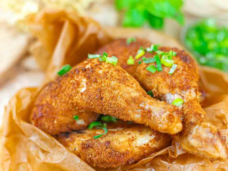 Two pieces of seasoned and baked chicken legs are garnished with chopped green onions and placed on brown parchment paper.