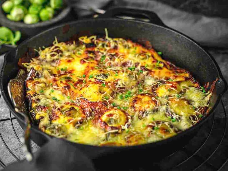 A cast iron skillet filled with a baked dish topped with melted cheese and herbs, resting on a cooling rack.