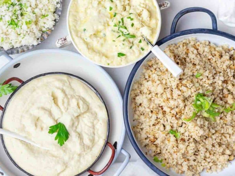 Four dishes of cauliflower-based sides, including mashed, creamed, and riced cauliflower, garnished with herbs, displayed on a white surface.