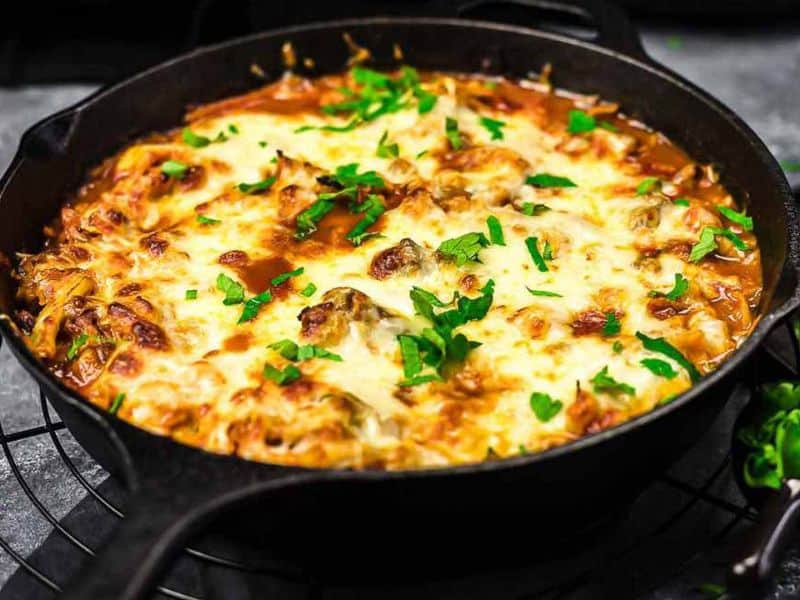 A skillet filled with baked lasagna topped with melted cheese and garnished with chopped parsley.