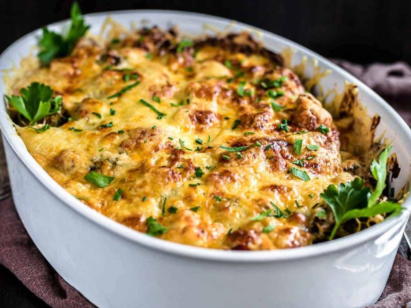 A baked casserole in a white dish topped with melted golden cheese and garnished with fresh parsley.
