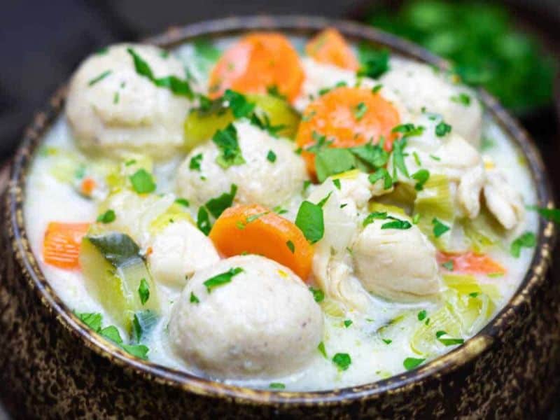 A bowl of chicken and vegetable soup with dumplings, garnished with chopped parsley.