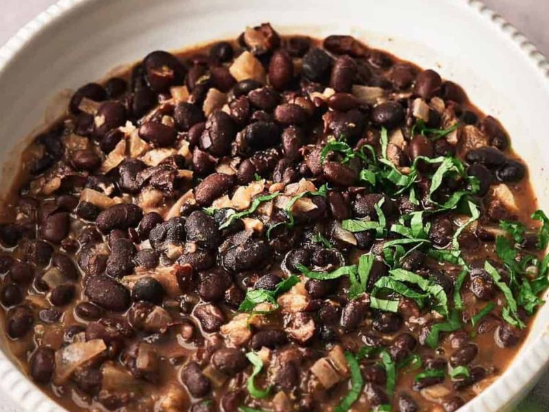 A bowl of cooked black beans with chopped herbs sprinkled on top, set in a white dish.