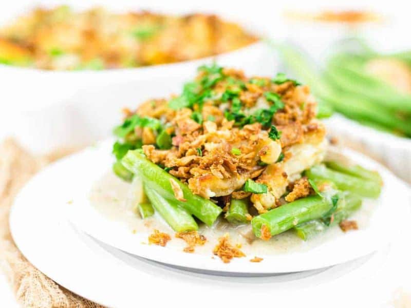A serving of green bean casserole topped with crispy fried onions and chopped herbs, plated on a white dish.