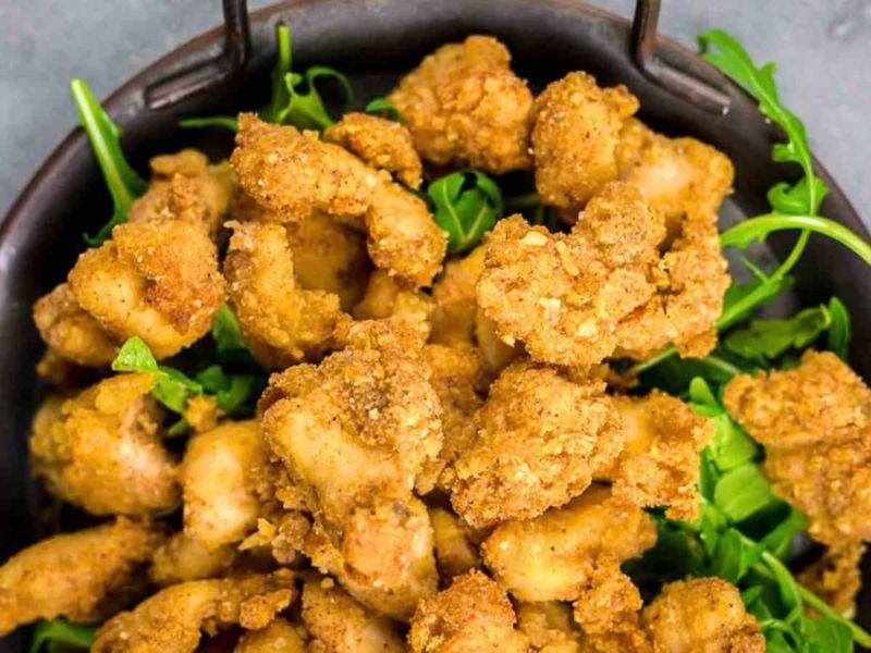 A bowl of golden-brown fried chicken bites served on a bed of fresh green arugula leaves.