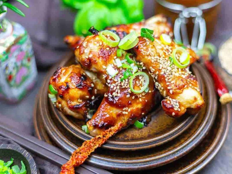 Grilled chicken drumsticks garnished with sesame seeds and sliced green onions, served on a brown plate.