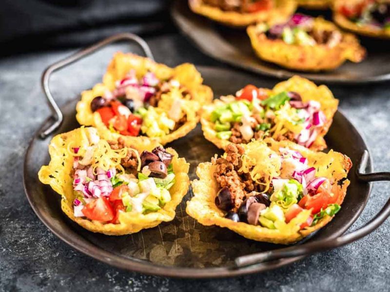 A metal plate with four taco salad cups made from crispy shells, filled with ground beef, lettuce, tomatoes, shredded cheese, onions, and black olives.