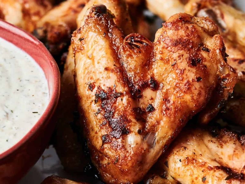 Close-up of seasoned, grilled chicken wings next to a bowl of creamy dipping sauce.