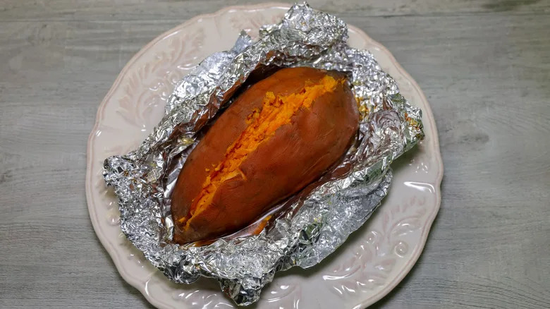An oven baked sweet potato wrapped in foil paper
