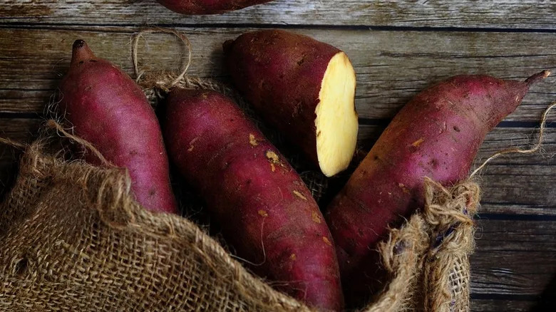 Sweet potatoes in a sack on wooden background