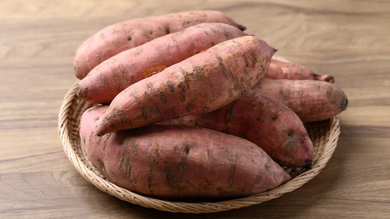 Raw organic Japanese sweet potatoes in basket on wooden background
