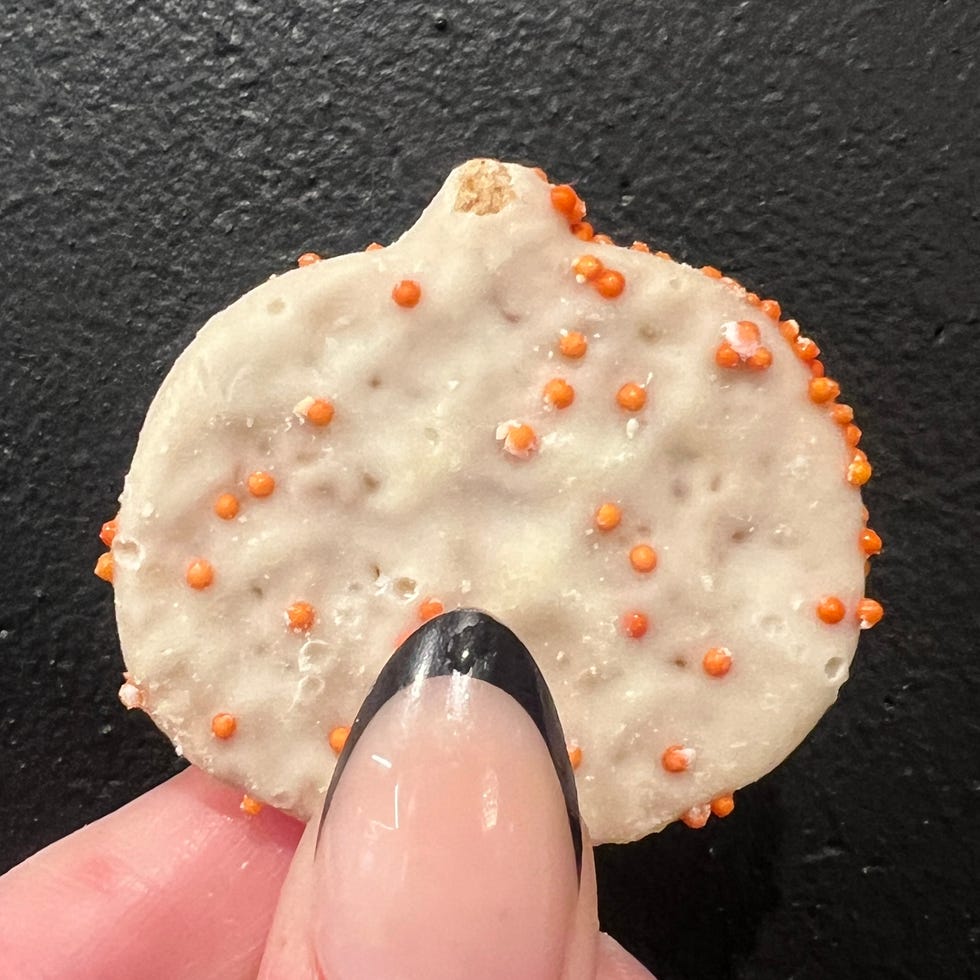 hand holding mini pumpkin shaped frosted cookie with sprinkles