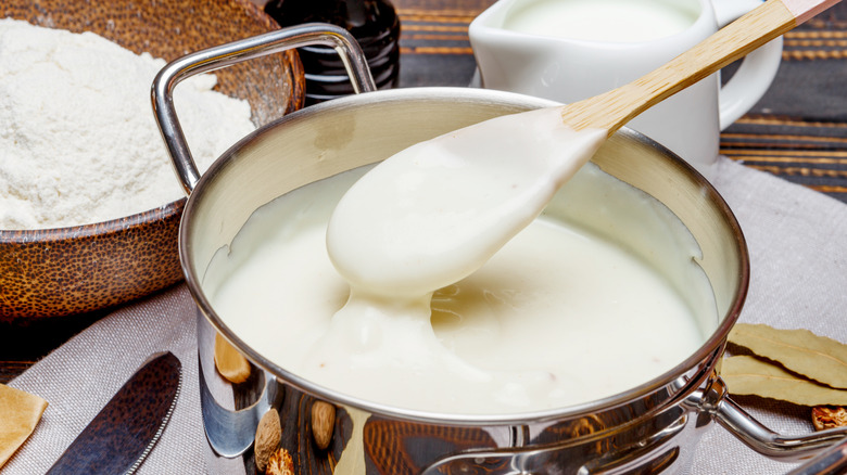 A pot of bechamel sauce being stirred with a wooden spoon