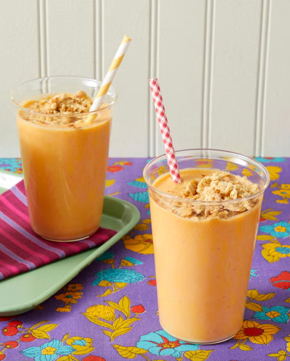 three cups of pumpkin smoothies topped with granola and straws on a colorful tablecloth