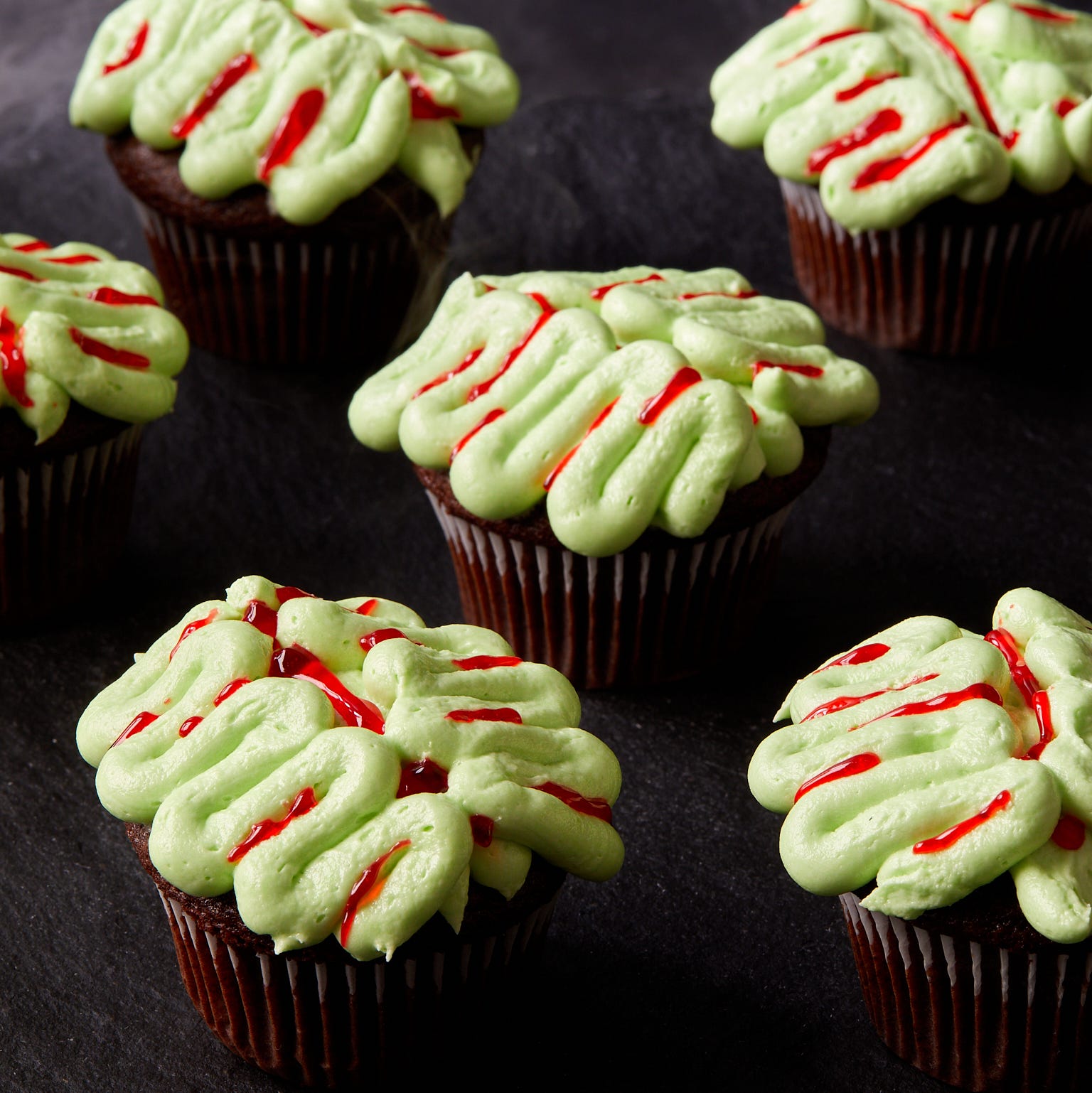 chocolate cupcakes decorated with green frosting and red gel food coloring to look like zombie brains