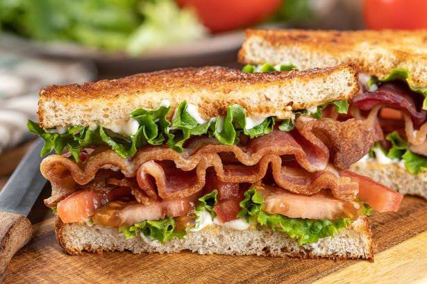 Closeup of blt sandwich made with bacon, lettuce and tomato on toasted whole grain bread cut in half on a wooden cutting board