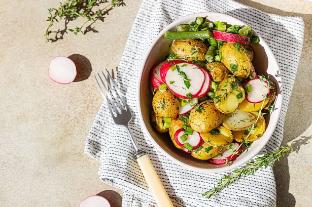 Tasty hot potato salad with green beans, fresh radishes and herbs dressing with olive oil and mustard sauce, light concrete background. Top view. Selective focus.