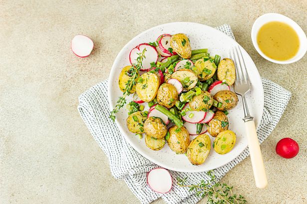 Tasty hot potato salad with green beans, fresh radishes and herbs dressing with olive oil and mustard sauce, light background.