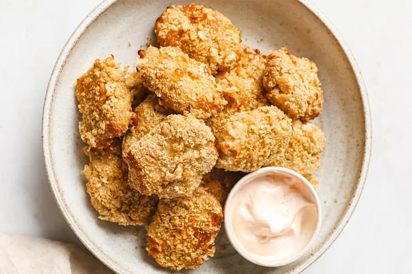 Chicken nuggets on a plate with a cup of dipping sauce.