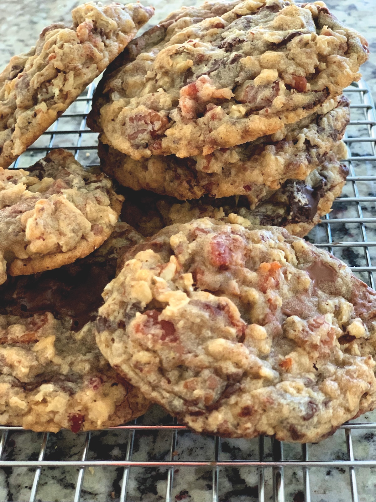 A stack of homemade oatmeal cookies with chocolate chips and visible chunks of ingredients, cooling on a metal wire rack.