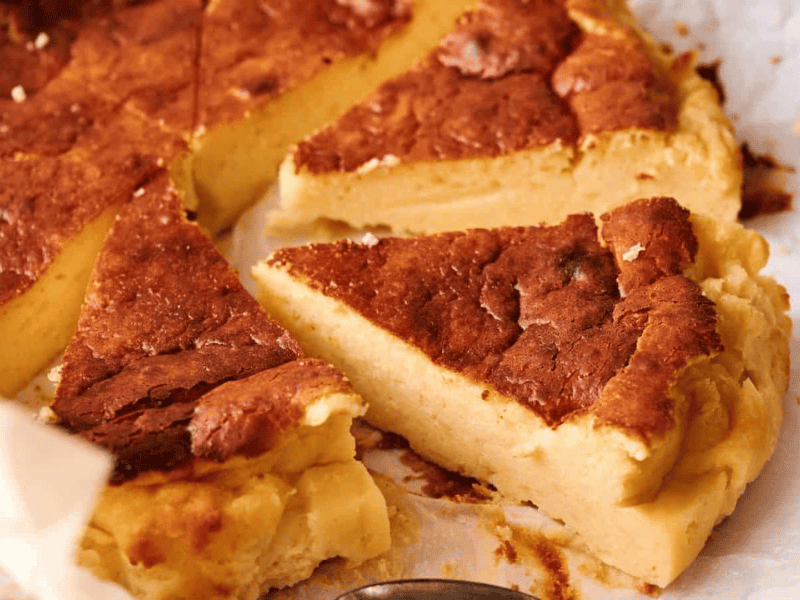 Close-up of a sliced, golden-brown cake with a dense, creamy texture on parchment paper.