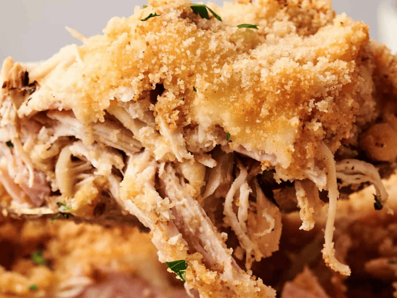 Close-up of a serving of shredded baked chicken topped with golden brown breadcrumbs and melted cheese.