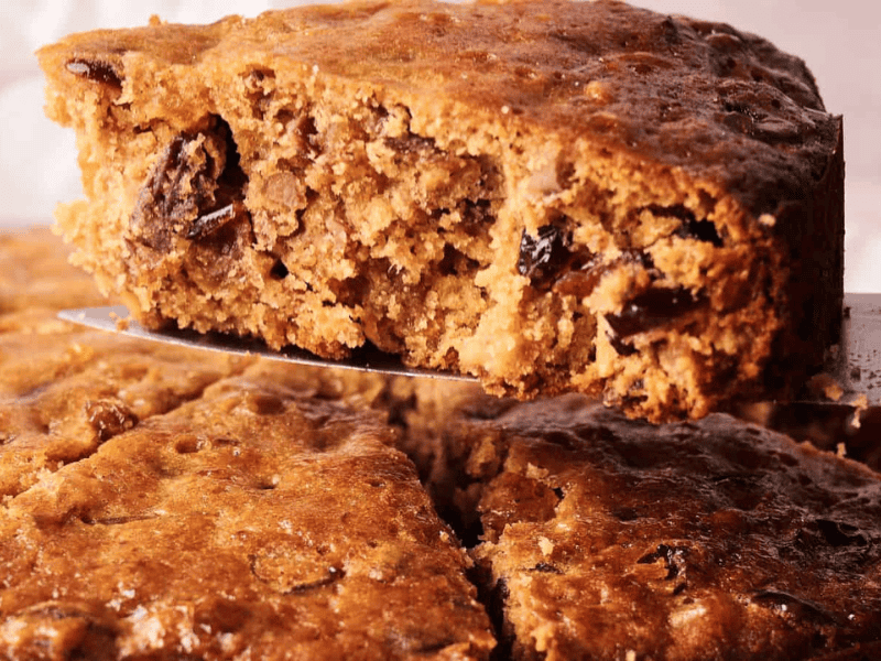 A close-up of a fruitcake being sliced, showing a dense, moist interior with visible pieces of dried fruit.