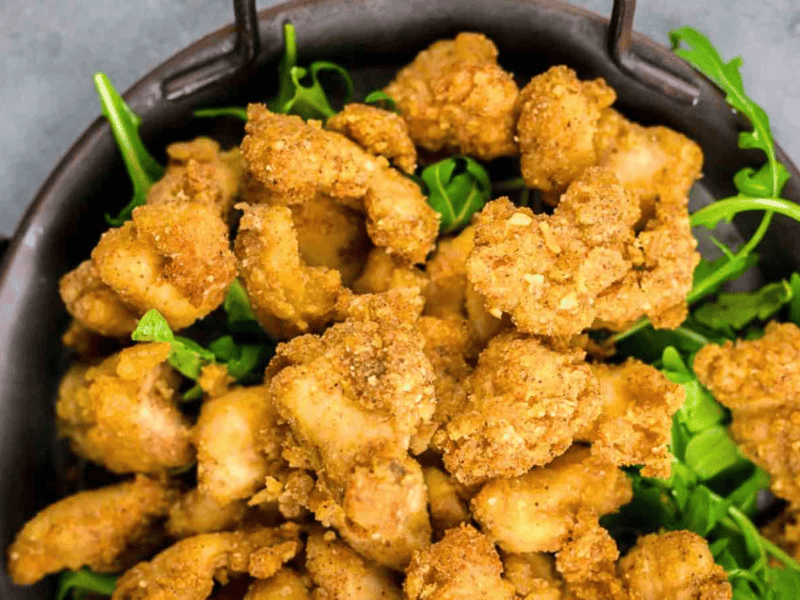 A bowl filled with crispy fried chicken pieces served on a bed of fresh green arugula leaves.