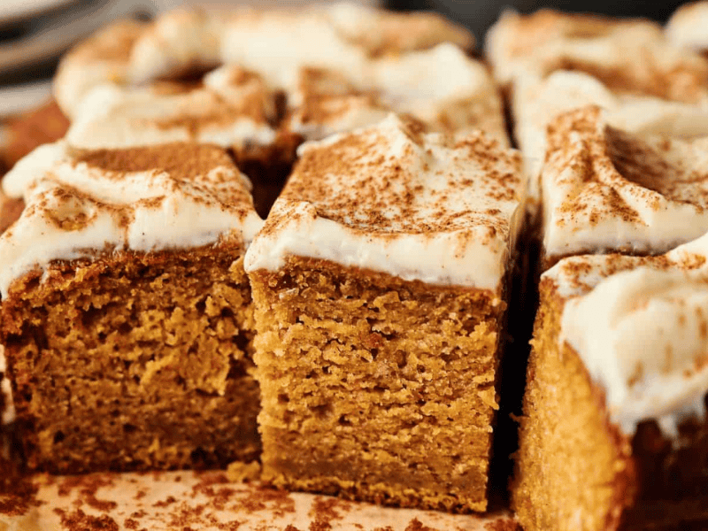 Close-up of sliced pumpkin cake with cream cheese frosting and a dusting of cinnamon on top.