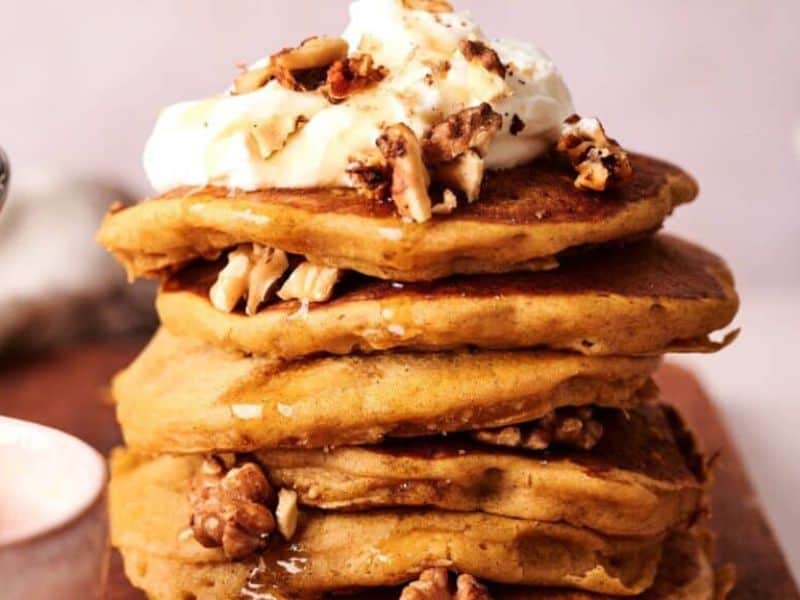 A stack of pancakes topped with whipped cream and chopped walnuts, with more walnuts between the layers.