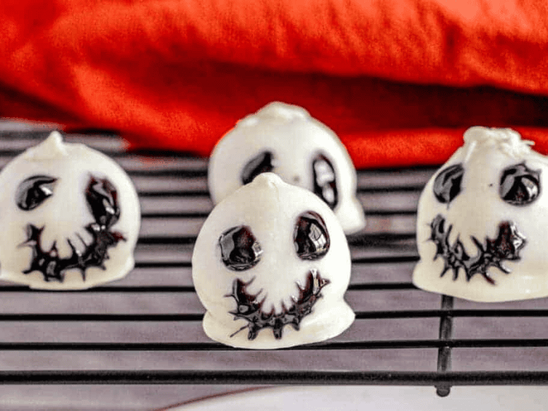 Four white meringue cookies decorated with black icing to resemble Jack Skellington faces, placed on a cooling rack.