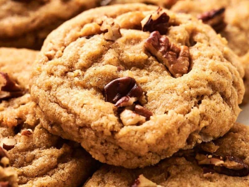 A close-up of several pecan cookies, showing their golden-brown color and pieces of chopped pecans on top.