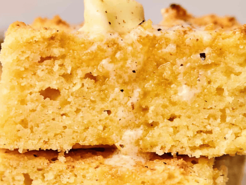 Close-up of two stacked slices of cornbread with a pat of melting butter on top.