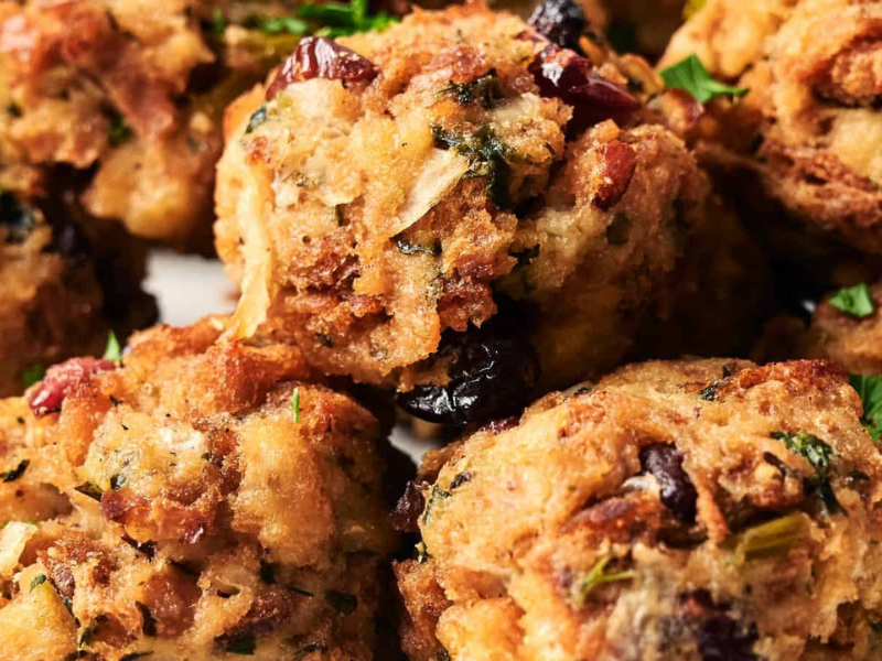 Close-up of baked stuffing balls with visible bread cubes, herbs, and dried cranberries.