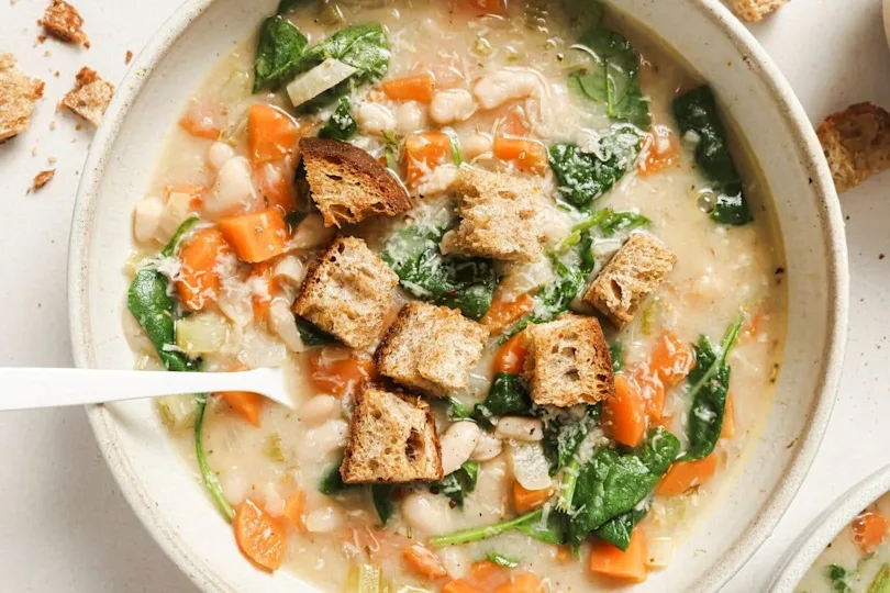 Creamy white bean soup served in a shallow bowl with spinach, carrots, and celery, topped with crunchy toasted bread cubes.