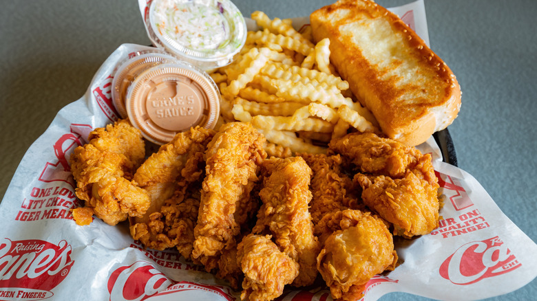 some boxes chicken fingers with fries, texas toast and sauce on a small table with a raising cane's placard