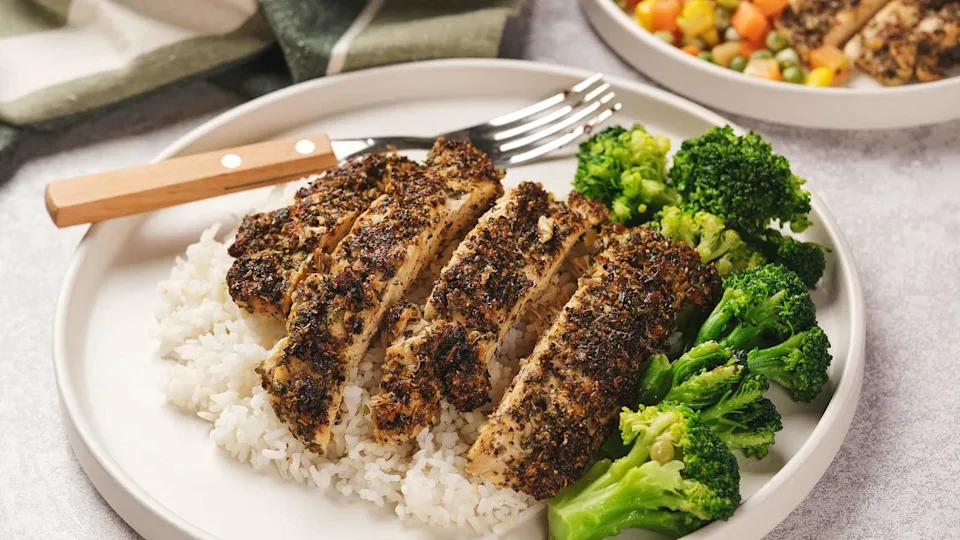 A plate with sliced herb-crusted chicken on rice, accompanied by broccoli.