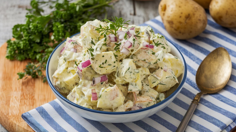 Bowl of potato salad topped with herbs and red onion