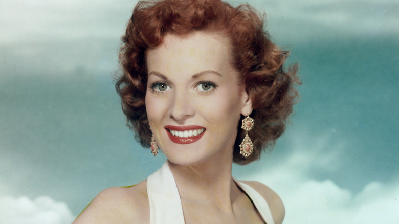 Maureen O'Hara smiling with a white top, dangling earrings, and red lipstick
