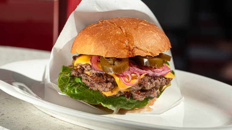 Cheeseburger on white plate with lettuce onions and peppers